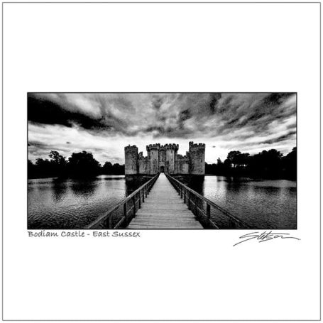 Black and white photograph of a castle bridge over water with dramatic clouds.