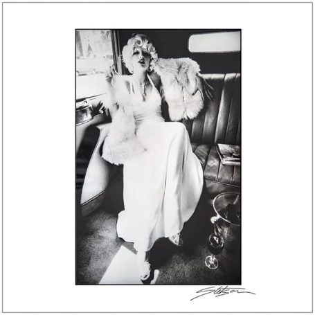 A woman in a vintage white dress sitting in a car, laughing joyfully.