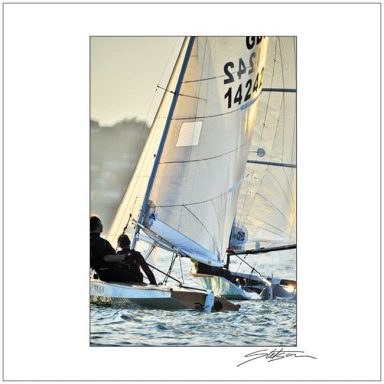 Sailboat with two people navigating on calm water during sunset.