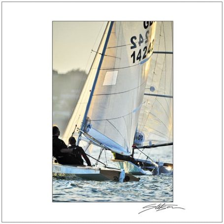Sailboat with two people navigating on calm water during sunset.