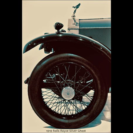 A close-up of a vintage car's front wheel with a detailed spoke pattern.