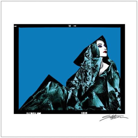 A woman in a dramatic green outfit poses against a bold blue background.