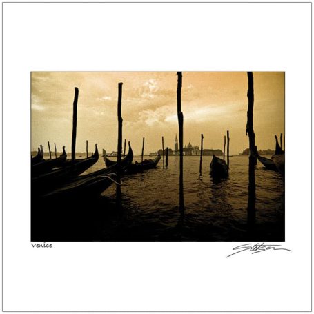 Silhouettes of boats and poles against a sunset sky reflecting on water.