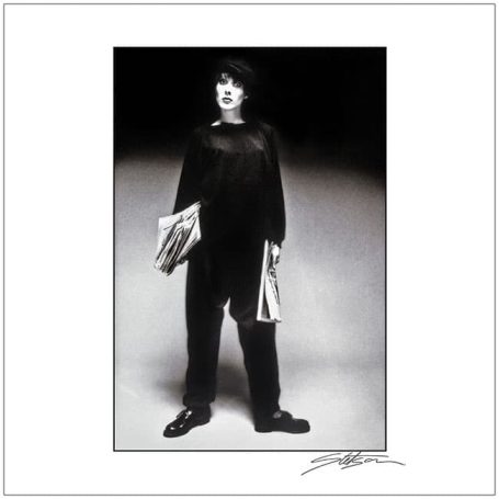 A person in black clothing standing with newspapers in hand.