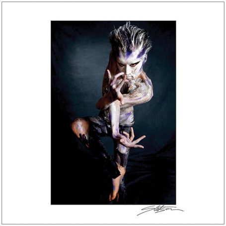 A figure with intricate body art poses dramatically against a dark background.