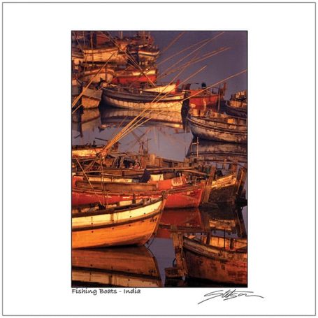Fishing boats with tall masts and nets docked in calm waters at sunset.