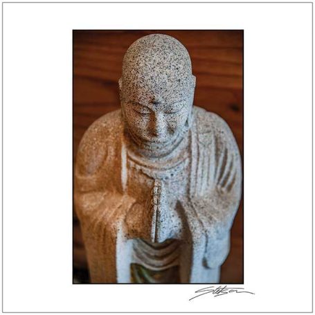 Stone statue of a Buddha figure with hands in a praying position.