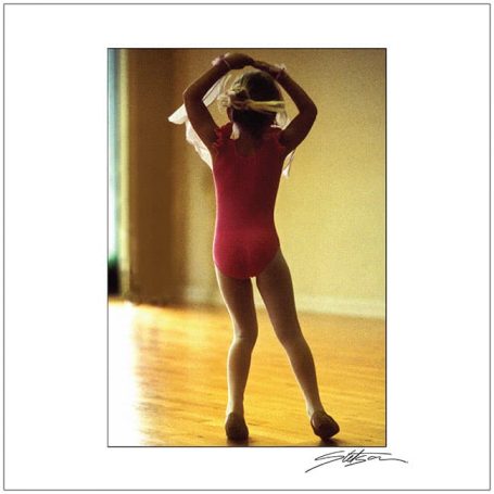 Ballet dancer in a red leotard, posing gracefully with arms raised.