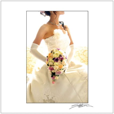 A bride in a strapless gown holding a floral bouquet, seated elegantly.