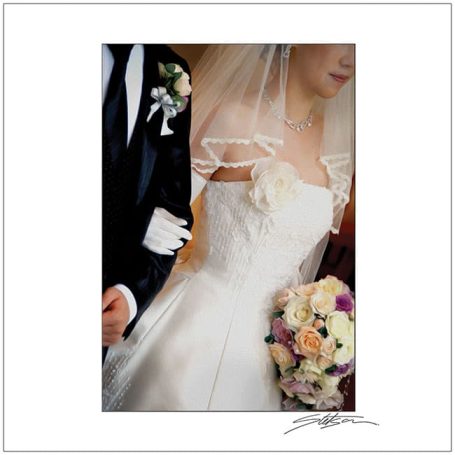Bridal gown detail with floral bouquet and a companion in formal attire.