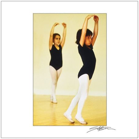 Two young ballet dancers in black leotards performing in a studio.