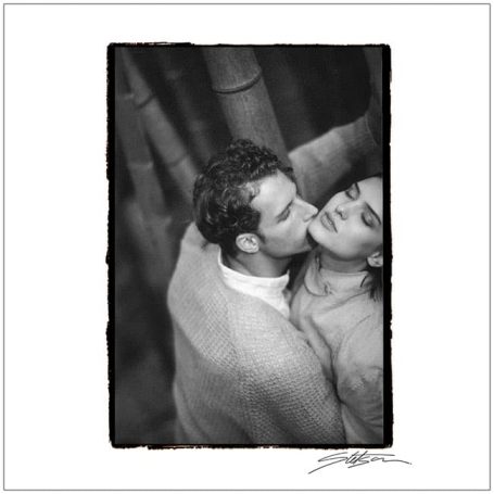 A black-and-white photo of a couple embracing among bamboo stalks.