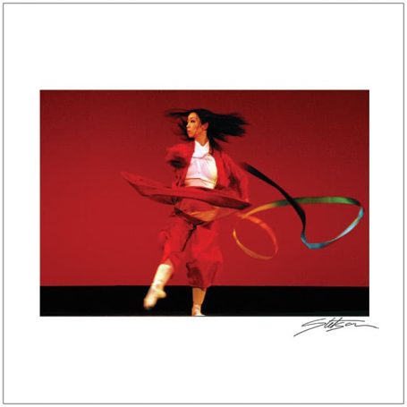 A dancer in a red outfit performs with flowing ribbons against a bold red backdrop.