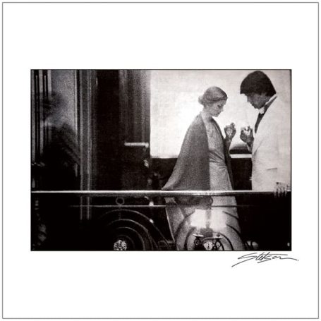 A gentleman and a lady conversing indoors, with a vintage aesthetic and soft focus.