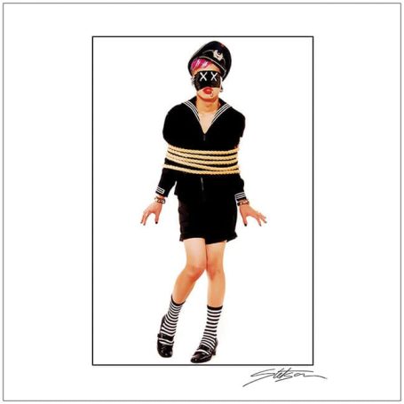Person in a black outfit, hands tied with rope, wearing a hat and striking a pose.