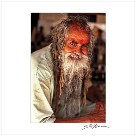 Smiling elderly man with long dreadlocks and a bushy beard, wearing a light-coloured shirt.