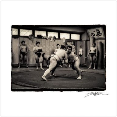 Two sumo wrestlers compete in a training session, surrounded by other wrestlers.