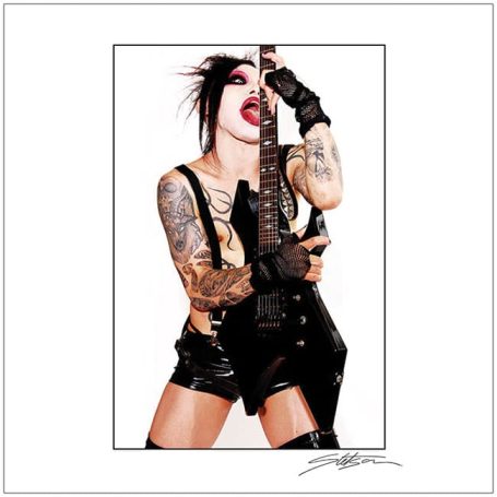 Tattooed musician in edgy attire poses with a guitar, sporting bold makeup and a fierce expression.