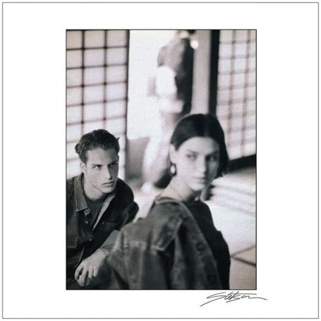 Black and white photograph featuring a man and a woman in traditional clothing, with blurred figures behind.