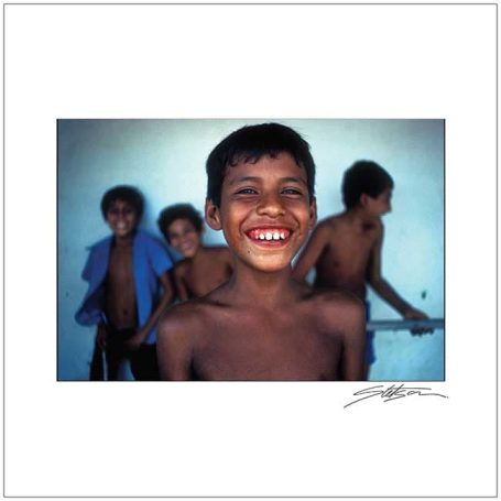 Smiling boy in front, with three other children in the background, all appearing cheerful.