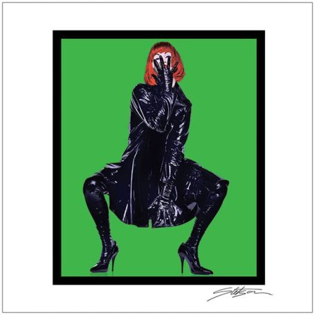 A person in a black outfit and red wig poses dramatically against a green background.