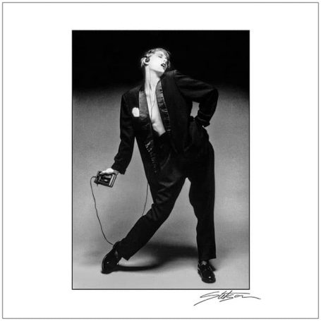 A person in a black suit poses dramatically, holding a camera.