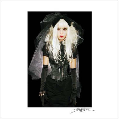 A woman in gothic attire with long blonde hair, dark gloves, and a black veil.