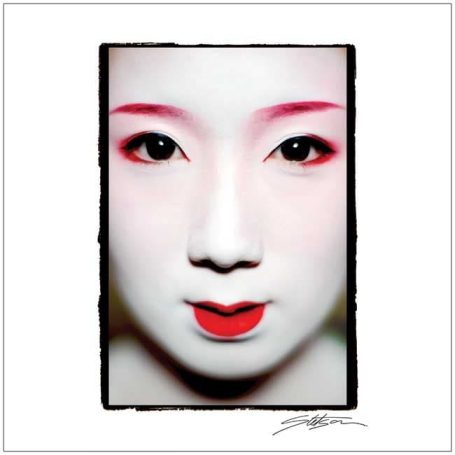 Close-up of a woman’s face with white makeup, red lips, and striking eye makeup.