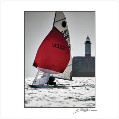 Sailing boat with a red sail near a lighthouse on a sunny day.