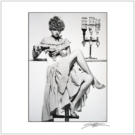A woman in a vintage dress sitting on a barstool, elegantly posing with a drink.