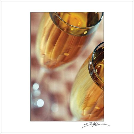 Two champagne flutes filled with golden bubbly drink, reflecting soft light.