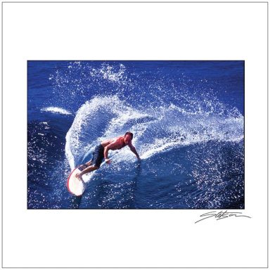 Surfer riding a wave, creating a splash in vibrant blue water.