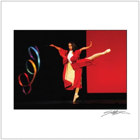 A ballet dancer in a red costume performing against a dark background with colourful rings.