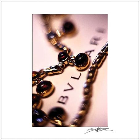 Close-up of a gold necklace with black stones against a Bvlgari background.