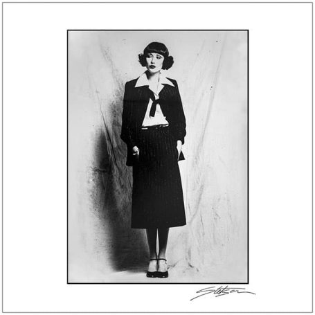 A young girl in 1920s fashion, wearing a bow tie and a skirt, standing against a plain backdrop.