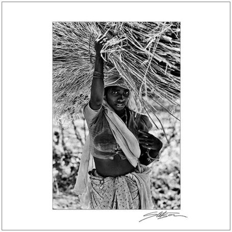 A woman holding a pot, standing beneath a woven canopy.