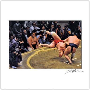 Two sumo wrestlers engaged in a match, with spectators watching in the background.