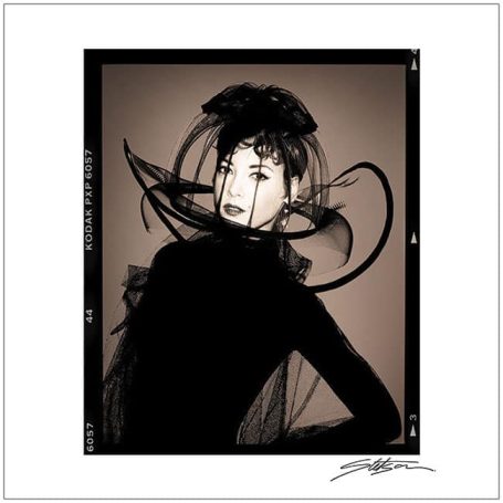 A woman in elegant black attire with artistic veils and a dramatic hat.
