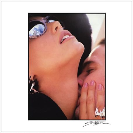A woman with sunglasses leans towards a man, sharing an intimate moment.