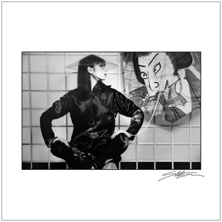 A person in traditional attire poses against a mural of a fierce character.