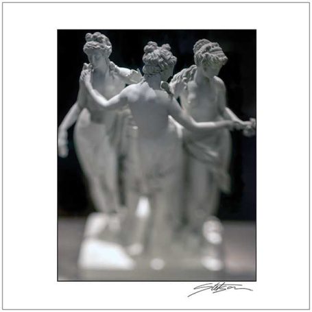 Three classical-style statues of female figures in a soft focus.