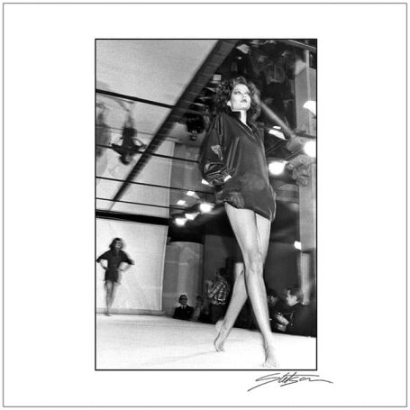 A model walking the runway in a stylish black outfit with sleek legs showcased.