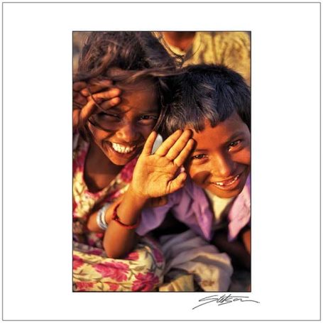 Two cheerful children smiling and waving, dressed in colourful clothing.