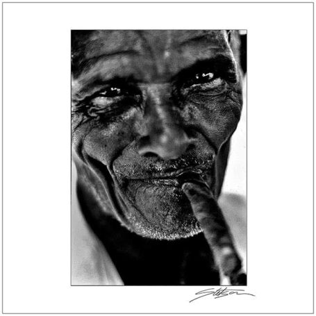 Close-up of an elderly man with a thoughtful expression, holding a finger to his lips.