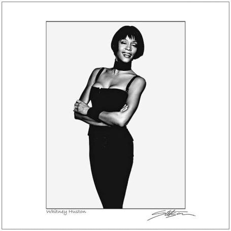 A woman in a black dress poses confidently, smiling with arms crossed.