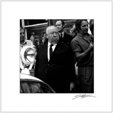 Alfred Hitchcock surrounded by a crowd, dressed in a suit, outdoors.