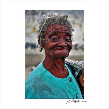 Elderly woman smiling, wearing a turquoise jacket, with white hair and warm expression.