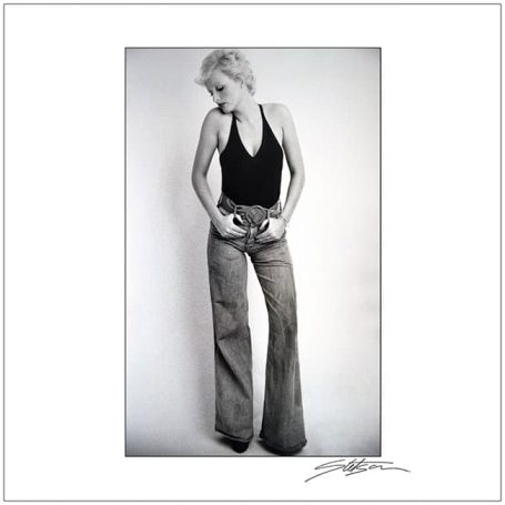 A woman in a black top and wide-leg trousers stands against a plain background.