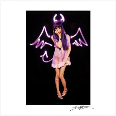 A person with purple hair poses playfully, wearing a light dress and devil horns.
