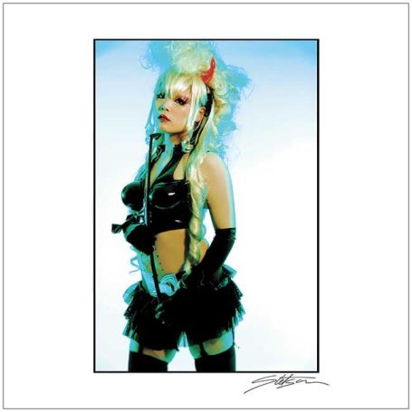 Person in edgy, alternative fashion with long blonde hair and bold accessories.